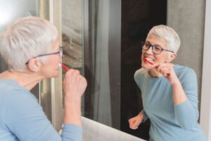 Mature woman brushing her teeth in front of mirror
