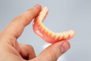 Person holding lower denture between two fingers