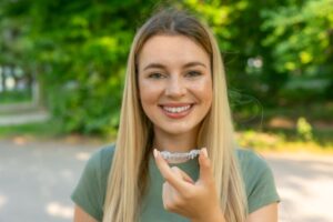 Smiling young woman holding an Invisalign aligner