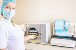 Woman in PPE using autoclave to sterilize dental instruments